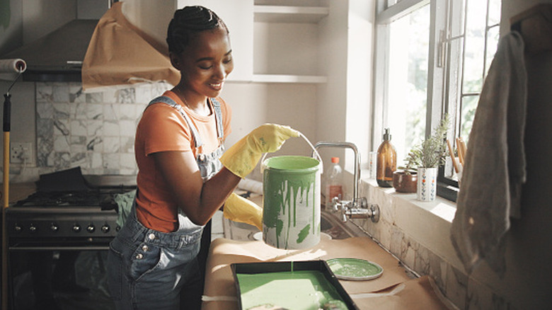 Woman pouring paint into tray in kitchen