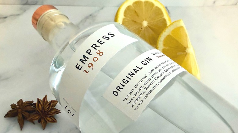 Bottle of Empress Original Gin laying down on a table, surrounded by lemon slices and star anise