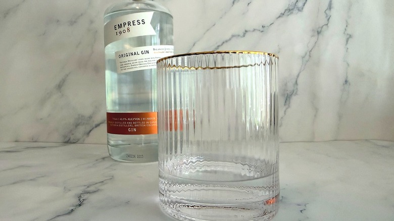 Empress 1908 gin in a glass, with the bottle in the background, all on a marble surface
