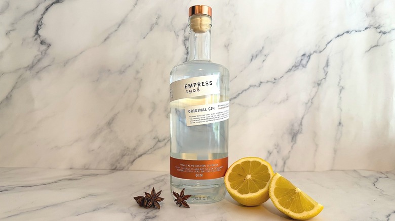 Bottle of Empress 1908 Original Gin next to sliced lemon and star anise on a marble surface