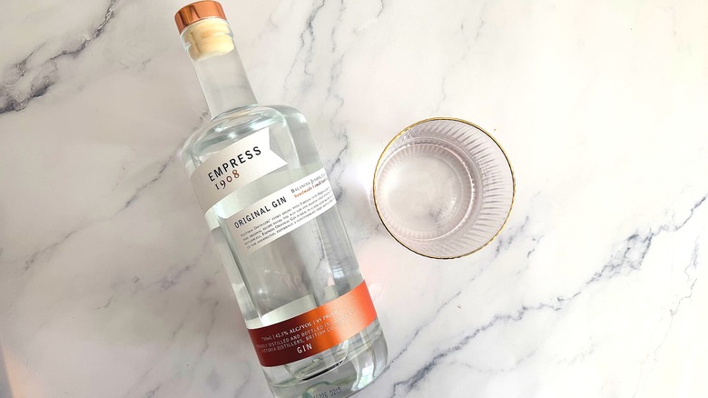 Top-down shot of an Empress 1908 Original Gin bottle next to a glass of gin on a marble surface