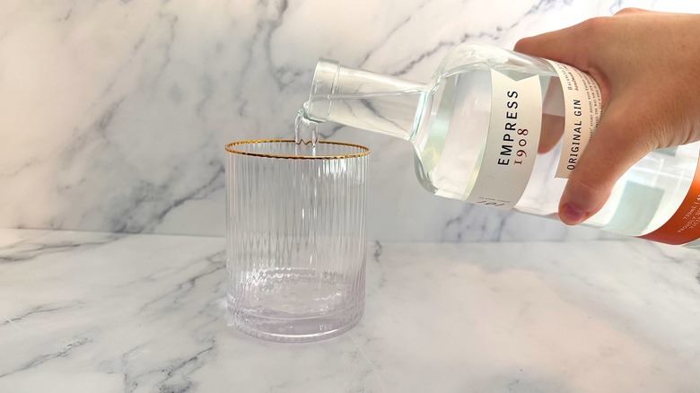 Hand pouring a bottle of Empress 1908 gin into a glass on a marble surface