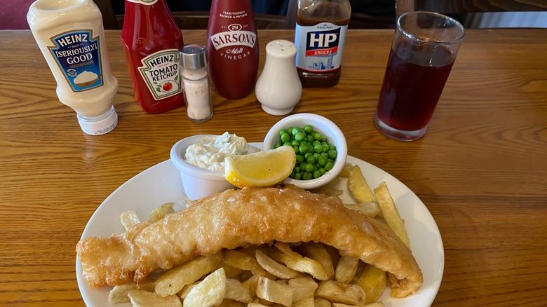 A plate of fish and chips with an array of condiments including HP size, malt vinegar, ketchup, mayonnaise, salt and pepper