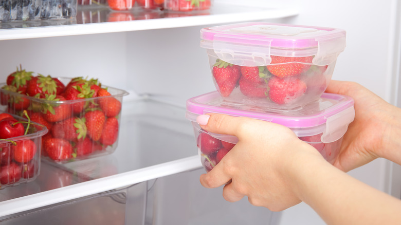 Hands placing two closed containers of strawberries into a refrigerator
