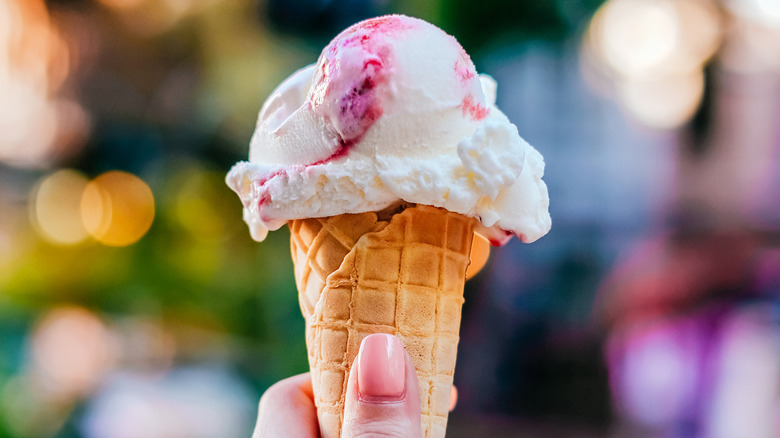 A hand holding vanilla cherry ice cream cone