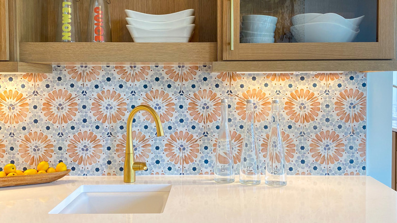 Unique floral tile backsplash with light wood cabinets.
