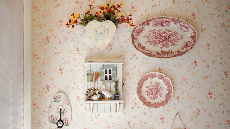A kitchen wall with floral wallpaper decorated with vintage plates and other cottagecore decor
