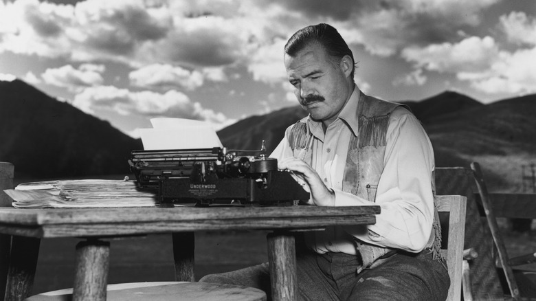Black and white photo of Ernest Hemingway sitting at a typewriter outside
