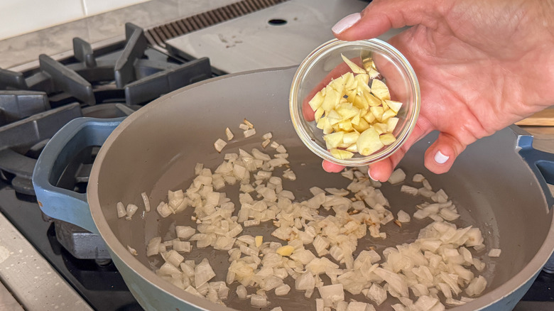 hand adding garlic to pan