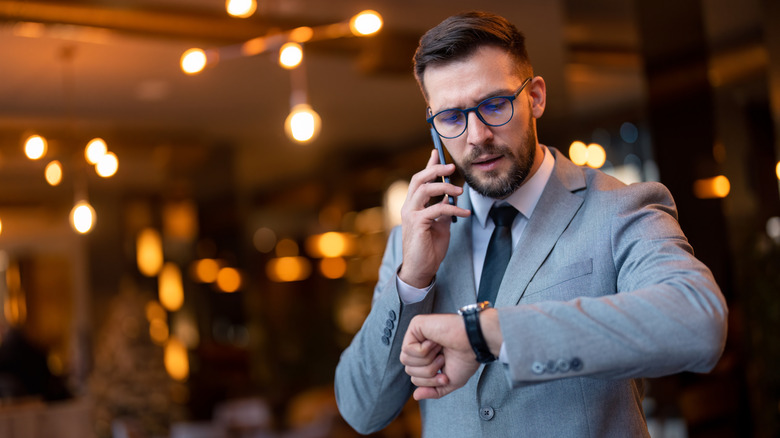 Man on the phone and looking at his watch with concern in a restaurant