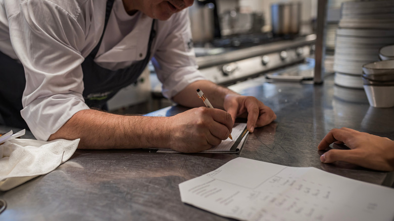Chef meeting with a patron and taking notes in a restaurant kitchen