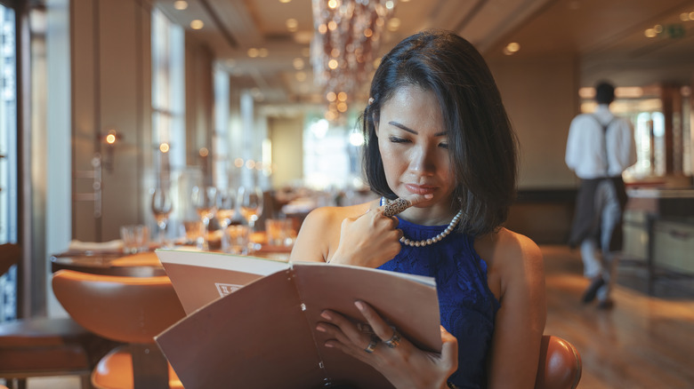 Woman in a blue dress and pearls thoughtfully reading a restaurant menu