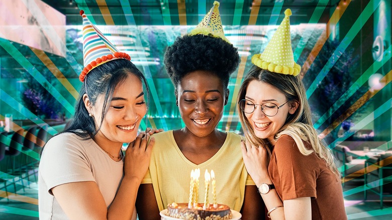 Three people gathered around a birthday cake against a backdrop of a restaurant interior and decorations
