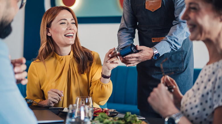 Woman in a mustard-colored blouse smiling and paying a restaurant bill