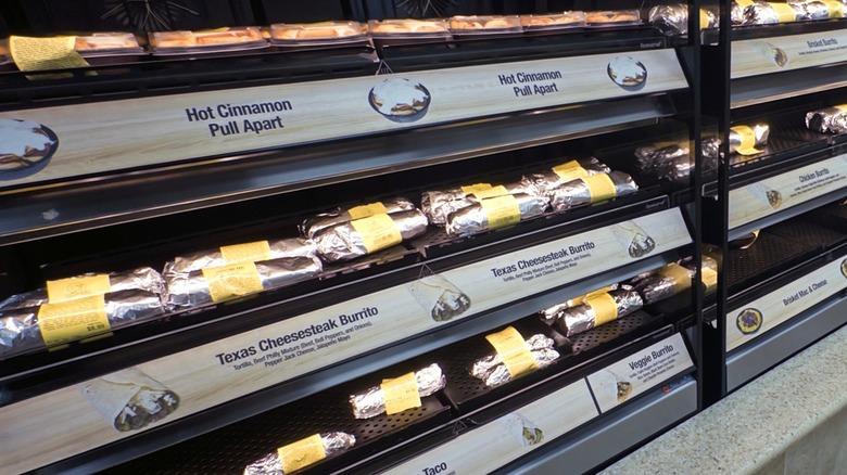 Shelves of hot food items at Buc-ee's including foil-wrapped cinnamon rolls, burritos, and tacos