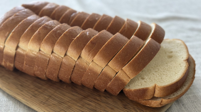 Sliced loaf of white miche bread on a wooden cutting board