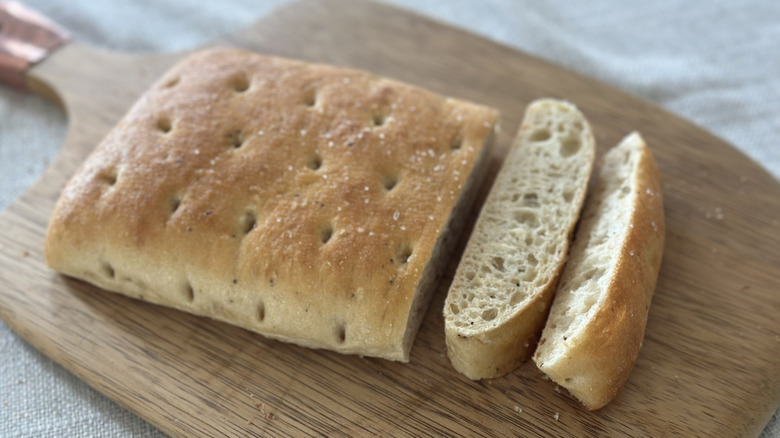 Rectangular loaf of focaccia bread on a wooden cutting board with two slices cut