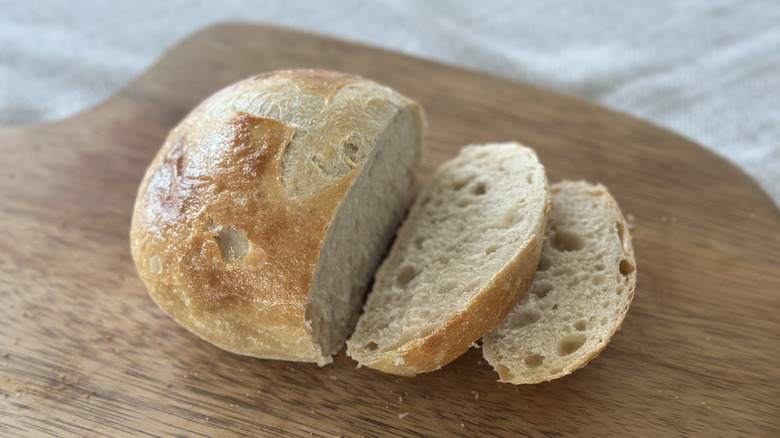 Round loaf of sourdough on a wooden cutting board with two slices cut