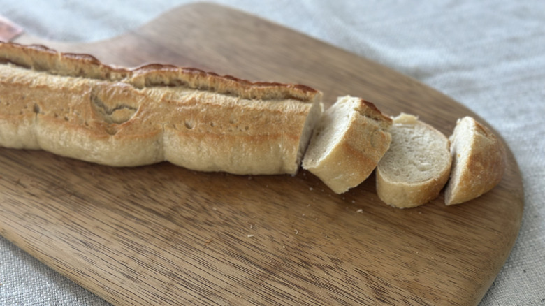 French baguette on a wooden cutting board with three slices cut