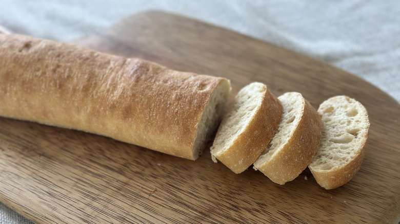 Small loaf of ciabatta on a wooden cutting board with three slices cut