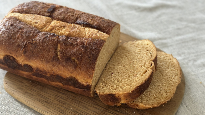 Loaf of tomato basil bread on a wooden cutting board with two slices cut