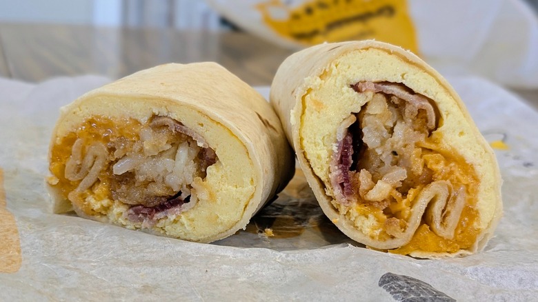 A cross section of a mini burrito with bacon, eggs, cheese and hashbrowns on a fast food wrapper
