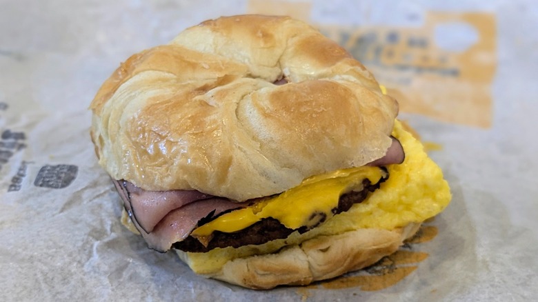 A bacon, ham, sausage, egg, and cheese croissant on a fast food wrapper