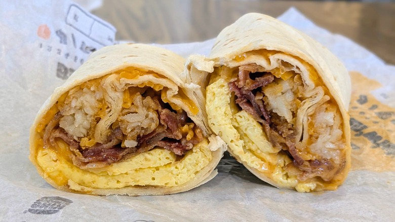 A cross section of a breakfast burrito with cheese, eggs, hashbrowns, and bacon on a fast food wrapper