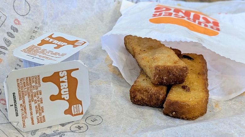 A package of three French toast sticks with two syrup packets on a fast food wrapper