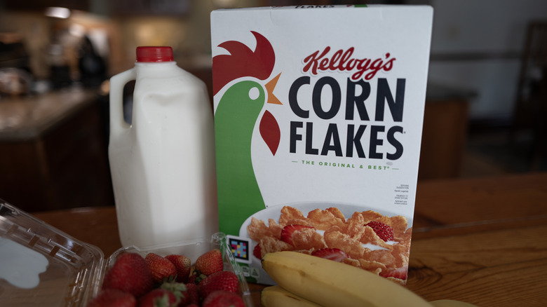 Box of Corn Flakes with bottle of milk, strawberries, and bananas on table