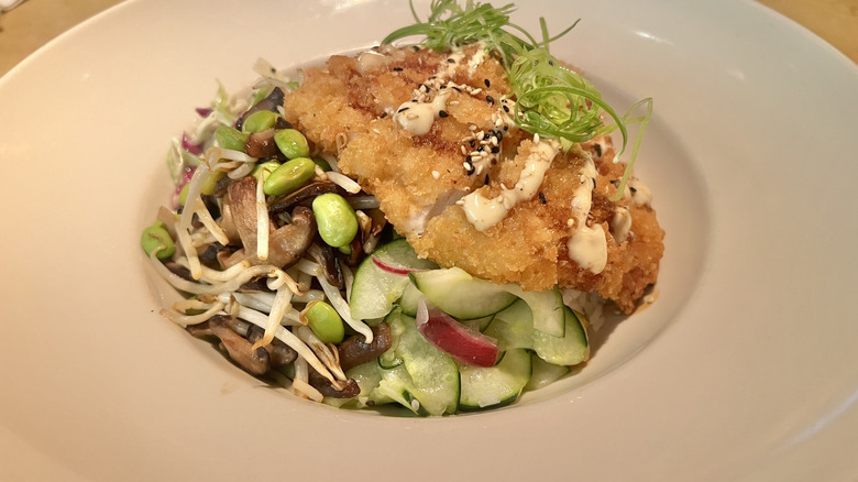 Katsu chicken dish close up on a plate topped with mayo, sesame seeds, and fresh herbs