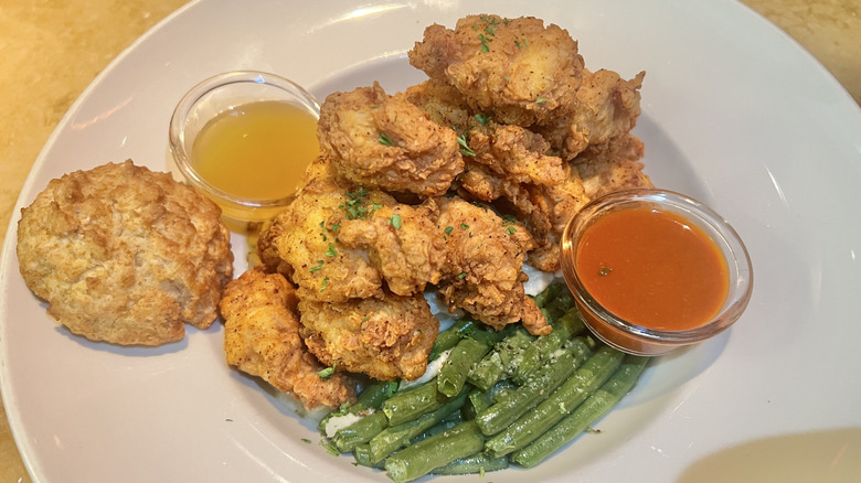 Fried chicken with beans, biscuit, beans, and sauces on a large white plate