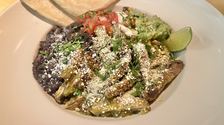 Carnitas bowl with fresh herbs, cheese, salsa, and a lime wedge on a large white plate