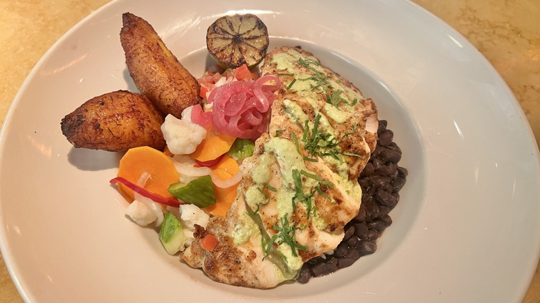 Peruviuan chicken bowl with plaintain and various garnishes in a white plate