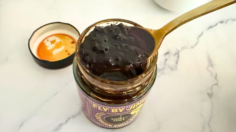 Spoonful of Fly By Jing Sweet & Spicy Chili Crisp held above jar of chili crisp on marble surface
