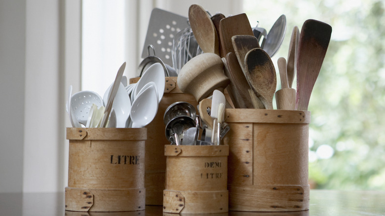 4 wooden pots full of kitchen cooking equipment like wooden spoons, spatulas, and can opener