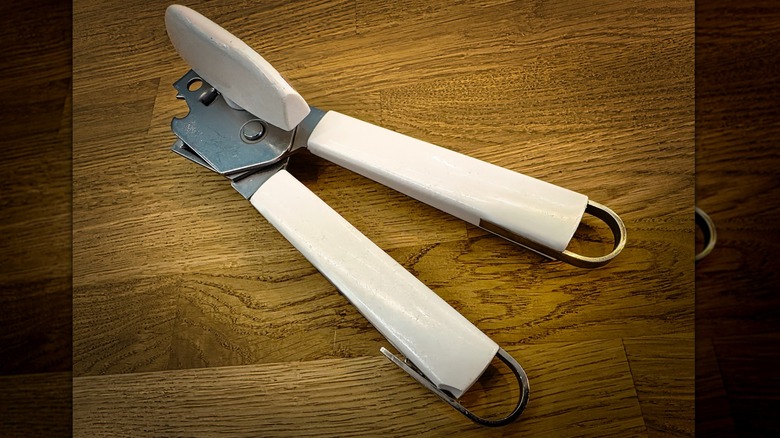 A white, manual can opener sitting on a wooden table