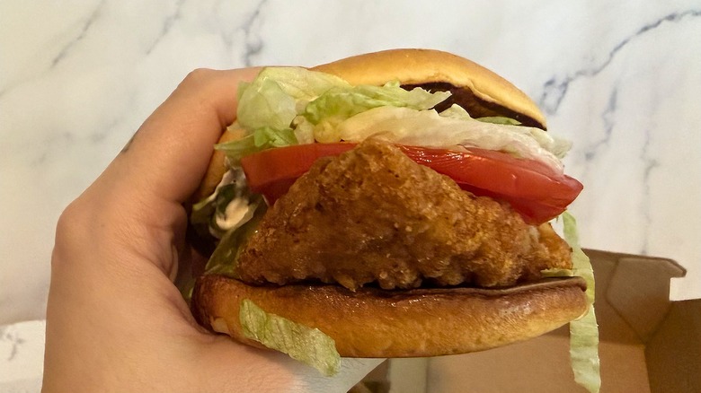 Hand holding McDonald's Deluxe McCrispy against marble background