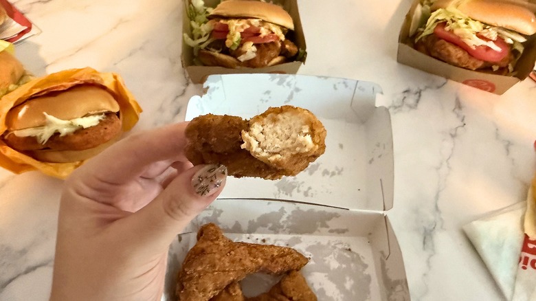 Hand holding part of McCrispy strip, several other McDonald's chicken items in background