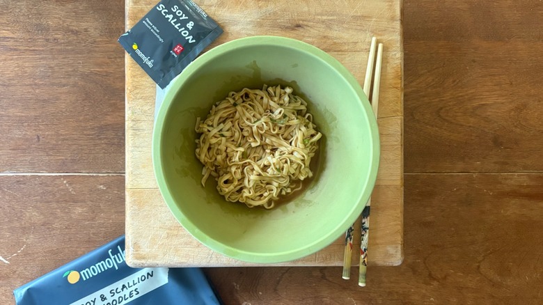 A green bowl filled with noodles on a wooden cutting board