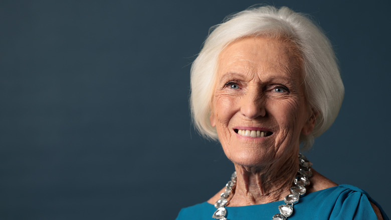 Former GBBO host Dame Mary Berry smiles and poses for a photo against a dark blue background