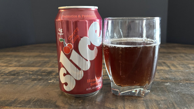 Slice cherry cola in can and glass on wooden table with black background