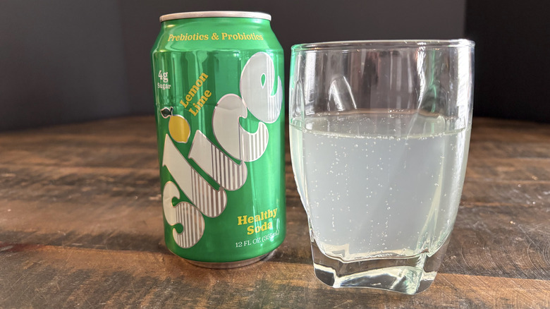 Slice lemon-lime soda in can and glass on wooden table with black background