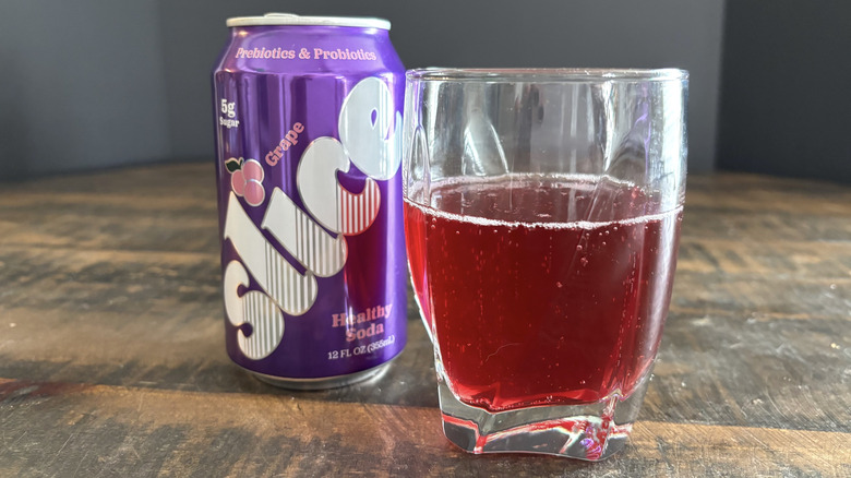 Slice grape soda in can and glass on wooden table with black background