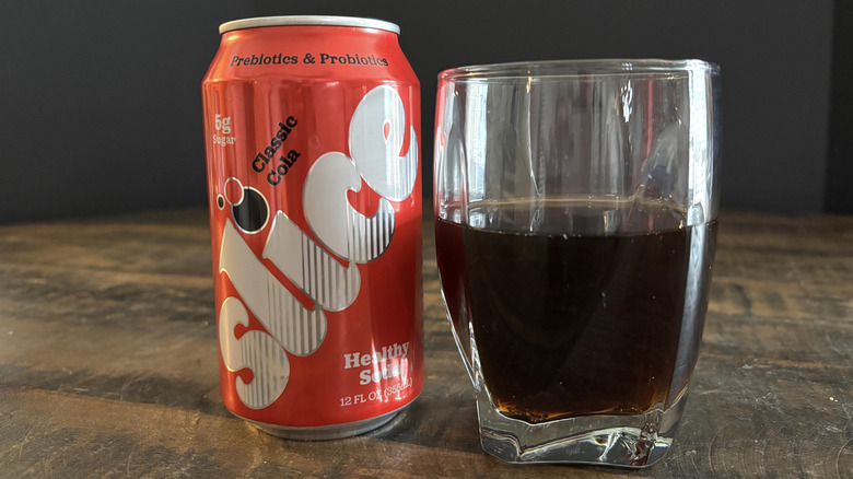 Slice classic cola in can and glass on wooden table with black background