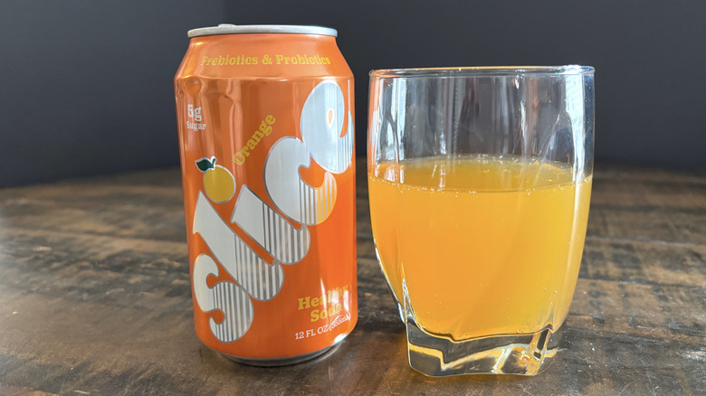 Slice orange soda in can and glass on wooden table with black background
