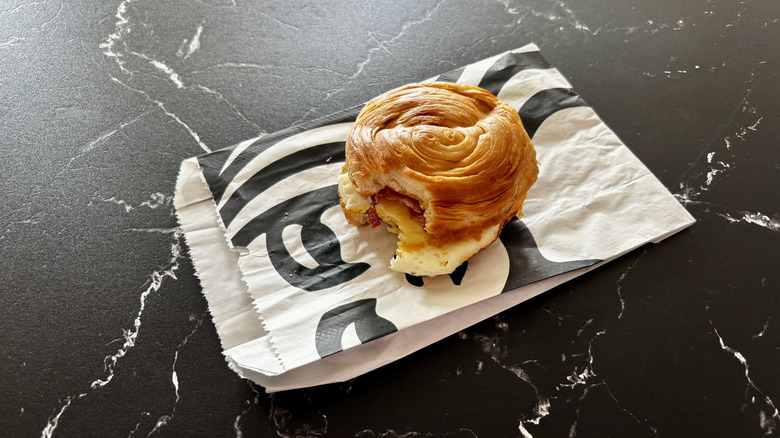 Starbucks bacon sandwich on croissant bun on wrapper on a black marble counter
