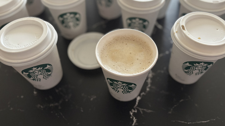 Various Starbucks hot latte cups on countertop with lid removed from one