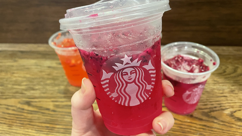 Hand holding the Mango Dragonfruit Refresher from Starbucks in front of other drinks on a table