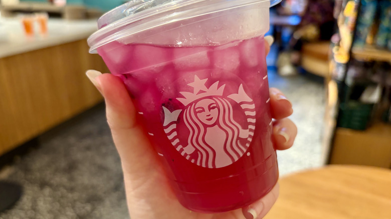 A hand holding a Starbucks Mango Dragonfruit Lemonade Energy Refresher